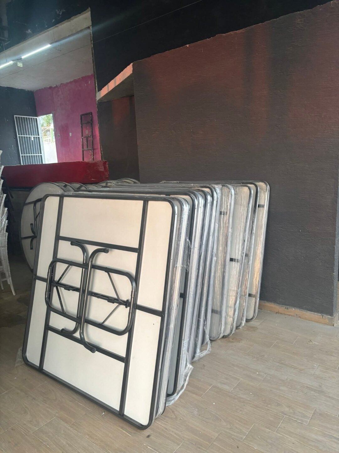 Mesas tablón plegadas y recargadas en fila, con cubierta clara y estructura negra