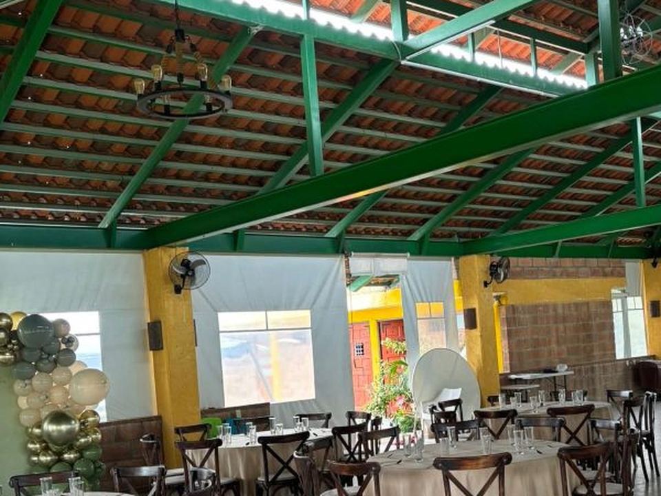 Montaje de evento con mesas redondas, mantel blanco y sillas Crossback bajo una palapa con estructura verde.
